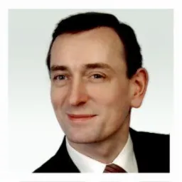 Portret mężczyzny w garniturze z krawatem na jasnym tle, skierowany lekko w lewo, z widocznymi zmarszczkami mimicznymi wokół oczu.