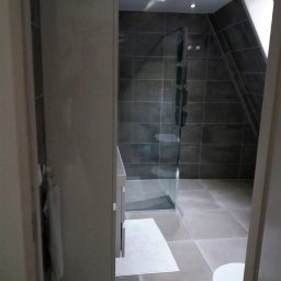 PABLO Paweł Wasąg - Nowoczesna łazienka z kabiną prysznicową ze szklanymi drzwiami, szarą glazurą, szafką z umywalką i ręcznikiem na wieszaku, oświetleniem punktowym i skośnym sufitem.