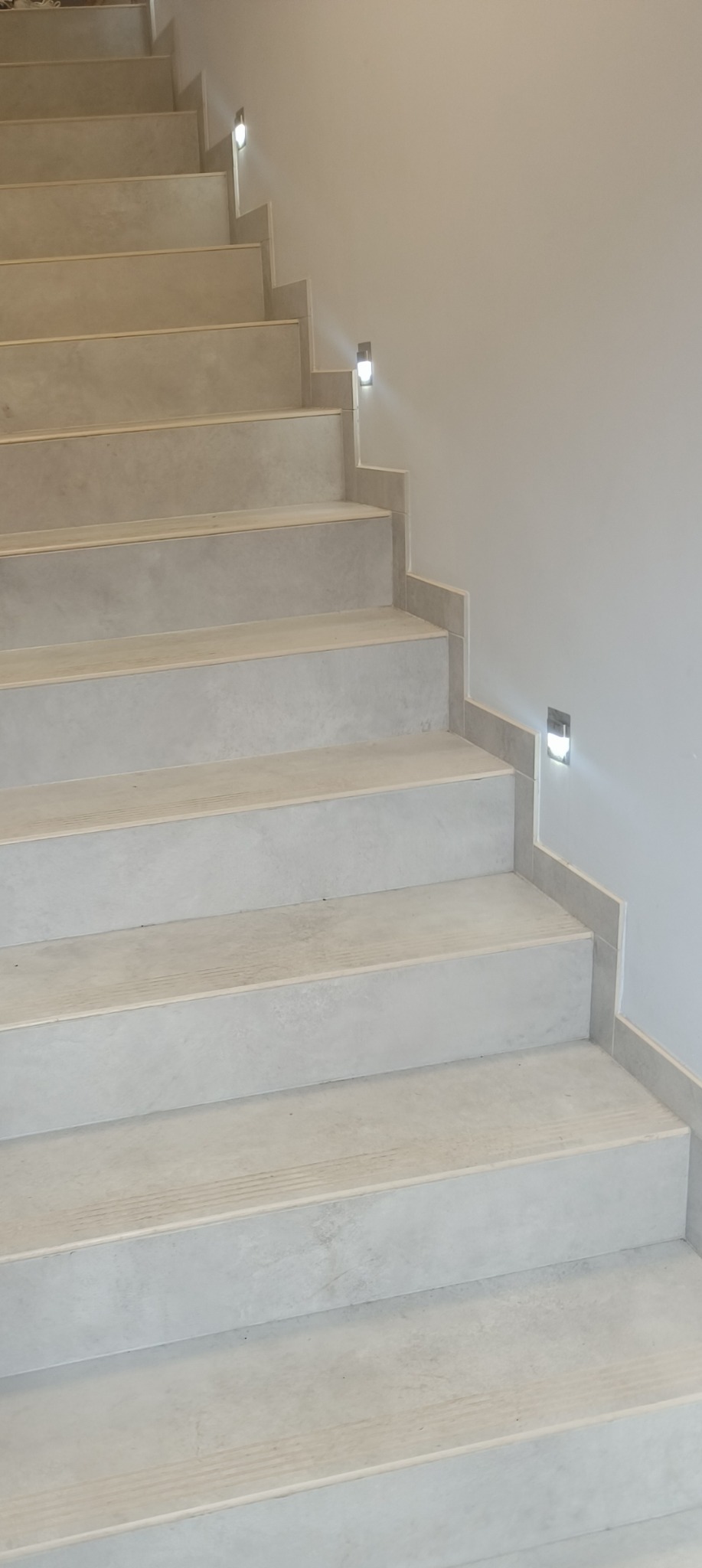 Schody wykończone szarym gresem z dyskretnym oświetleniem LED w ścianie.