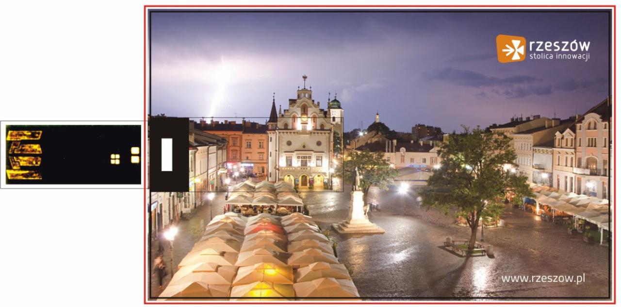 Rynek w Rzeszowie nocą, widok z góry, błyskawica na niebie, logo miasta w prawym górnym rogu.