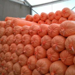 Stos pomarańczowych i białych bel tkanin w magazynie, zapakowanych w folię i związanych sznurkiem.