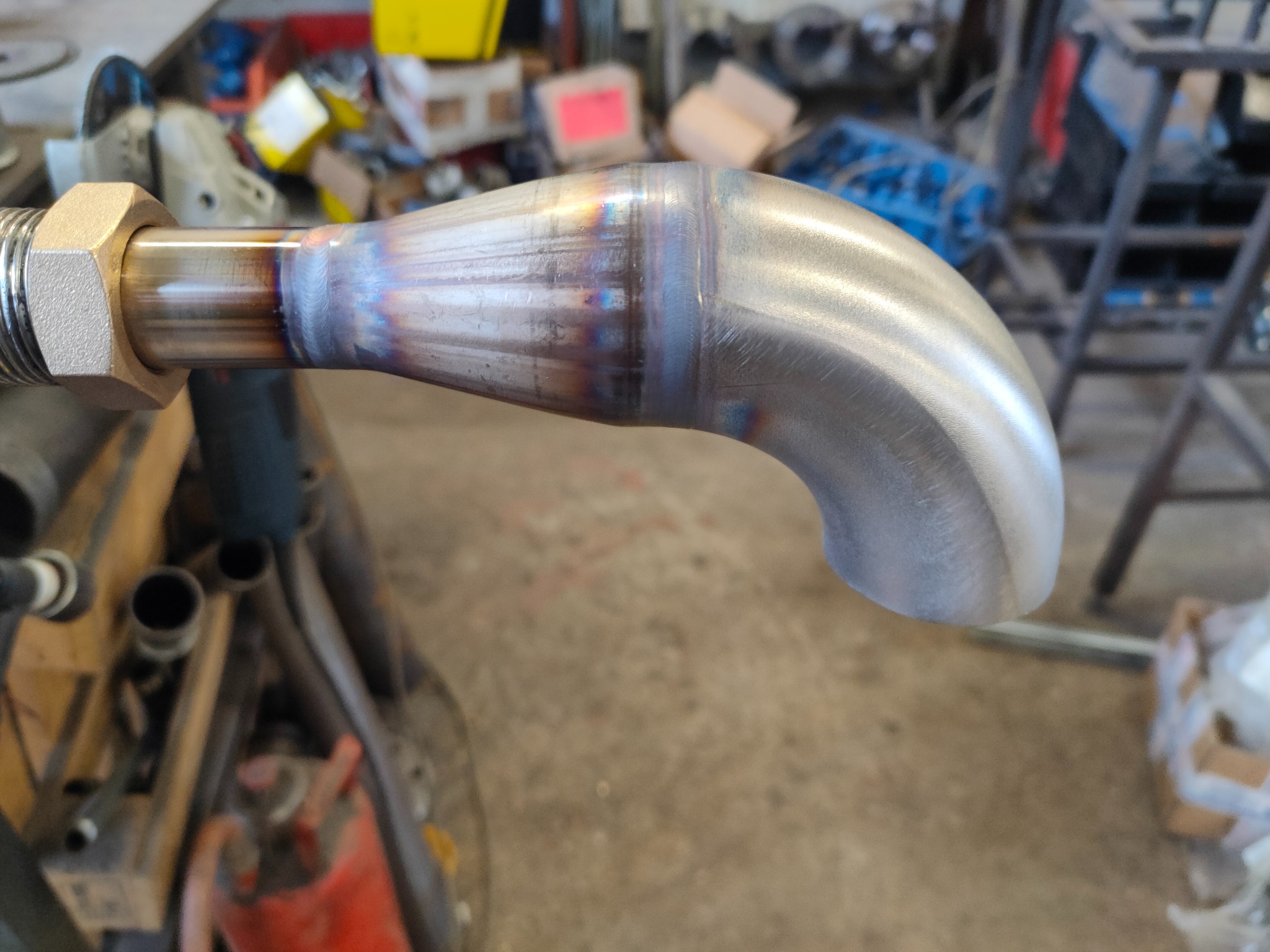 Metalowa rura z precyzyjnym spoiwem po obróbce, widoczne charakterystyczne przebarwienia termiczne, zakończona gwintem z nakrętką, w tle warsztat.