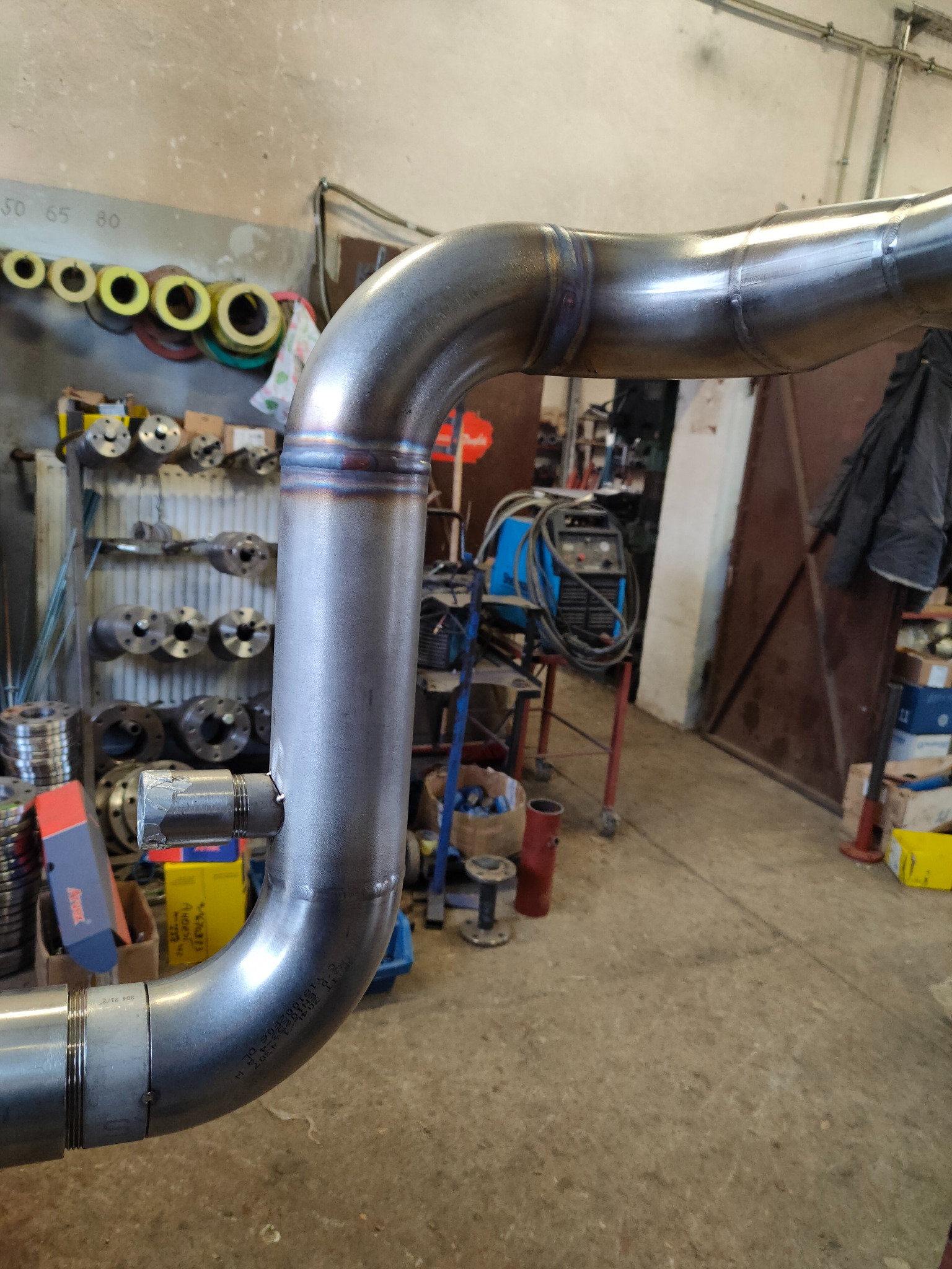 Precyzyjne spawy na rurze ze stali nierdzewnej, wykonane przez specjalistę z Brzezin. Widoczne ślady spawania i akcesoria warsztatowe w tle.