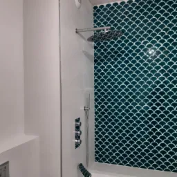 Wyremontowana łazienka z wanną i prysznicem deszczownicą, ściana wyłożona turkusową glazurą w kształcie rybiej łuski, chromowana armatura.