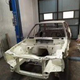 Karoseria samochodu po usunięciu rdzy i przygotowaniu do malowania, widoczna na podnośniku warsztatowym, z elementami konstrukcyjnymi w kolorze białym.