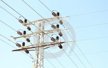 Słup wysokiego napięcia z izolatorami ceramicznymi na tle błękitnego nieba, widoczne liczne przewody elektryczne. Lekkie pochylenie słupa w prawo.