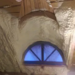 Poddasze budynku jednorodzinnego ocieplone pianką PUR, widoczne drewniane elementy konstrukcyjne i półokrągłe okno zabezpieczone folią.