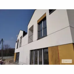 Nowoczesny dom w trakcie wykończenia elewacji, widoczne fragmenty ocieplenia, jasna kolorystyka i duże okna.