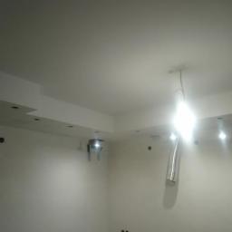 Dawid Świercz - Świeżo pomalowane wnętrze z ozdobnymi elementami sufitowymi, widoczne otwory pod oświetlenie punktowe i wystające kable elektryczne, sugerujące etap wykończeniowy.