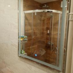 Dawid Świercz - Nowoczesna łazienka z kabiną prysznicową, widoczna w lustrze z podświetleniem LED, drewnopodobne płytki na ścianach kabiny, beżowe płytki imitujące marmur na pozostałych ścianach.