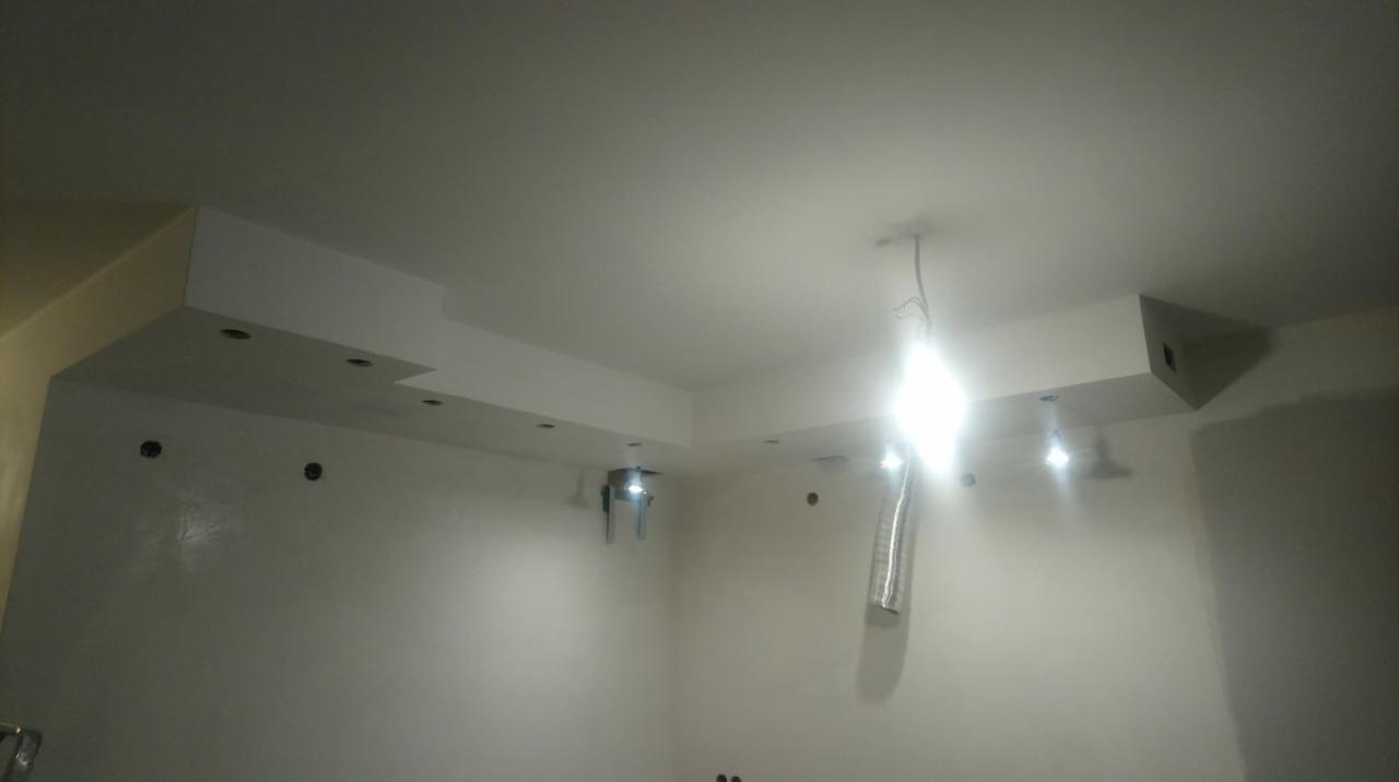 Świeżo pomalowane wnętrze z ozdobnymi elementami sufitowymi, widoczne otwory pod oświetlenie punktowe i wystające kable elektryczne, sugerujące etap wykończeniowy.