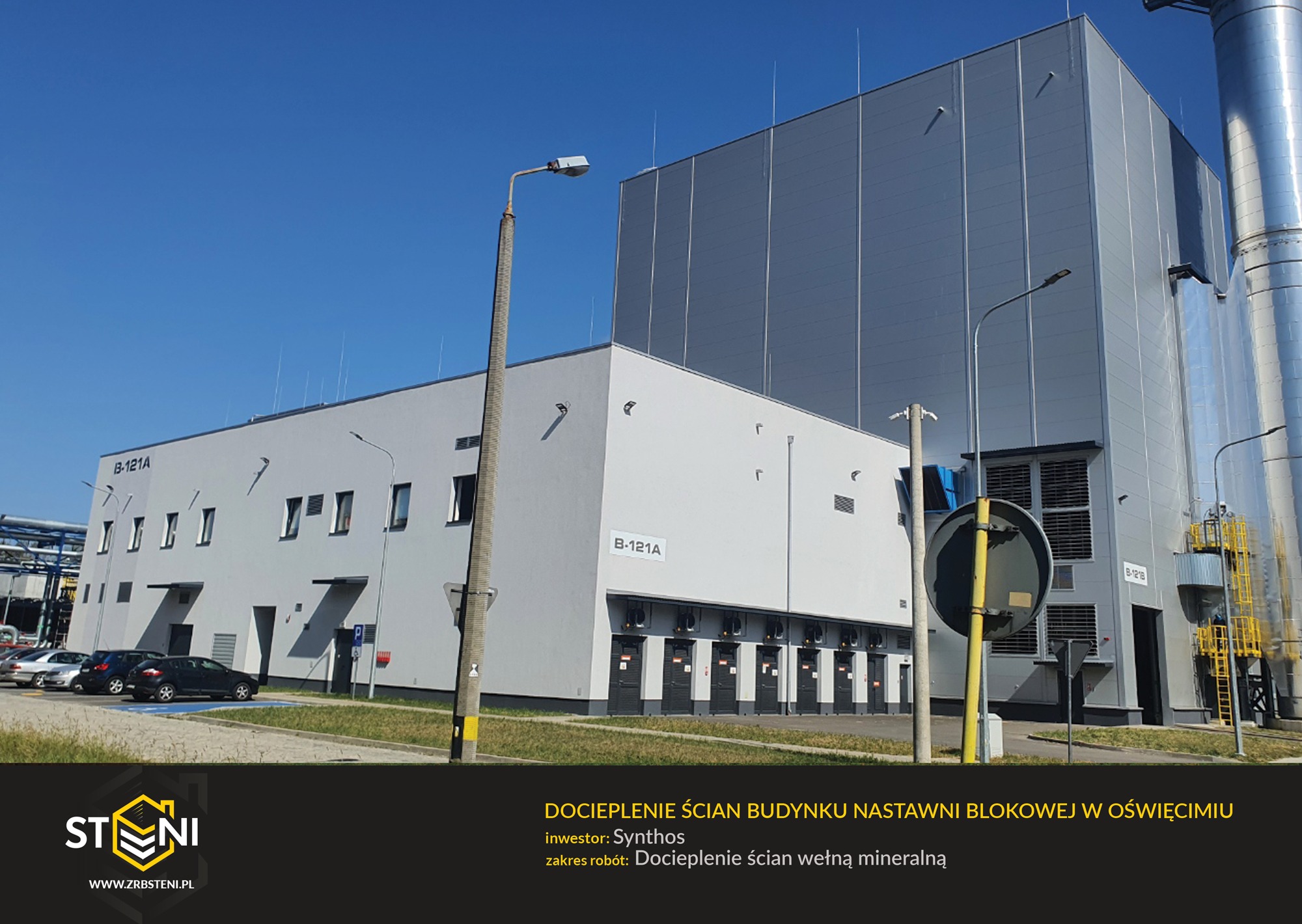 Szary budynek przemysłowy z docieplonymi ścianami, widoczne elementy instalacji i zaparkowane samochody, błękitne niebo w tle.