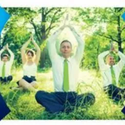 Grupa osób w strojach biznesowych, siedzących na trawie w pozycji lotosu z uniesionymi rękami w geście medytacji, na tle zieleni drzew.