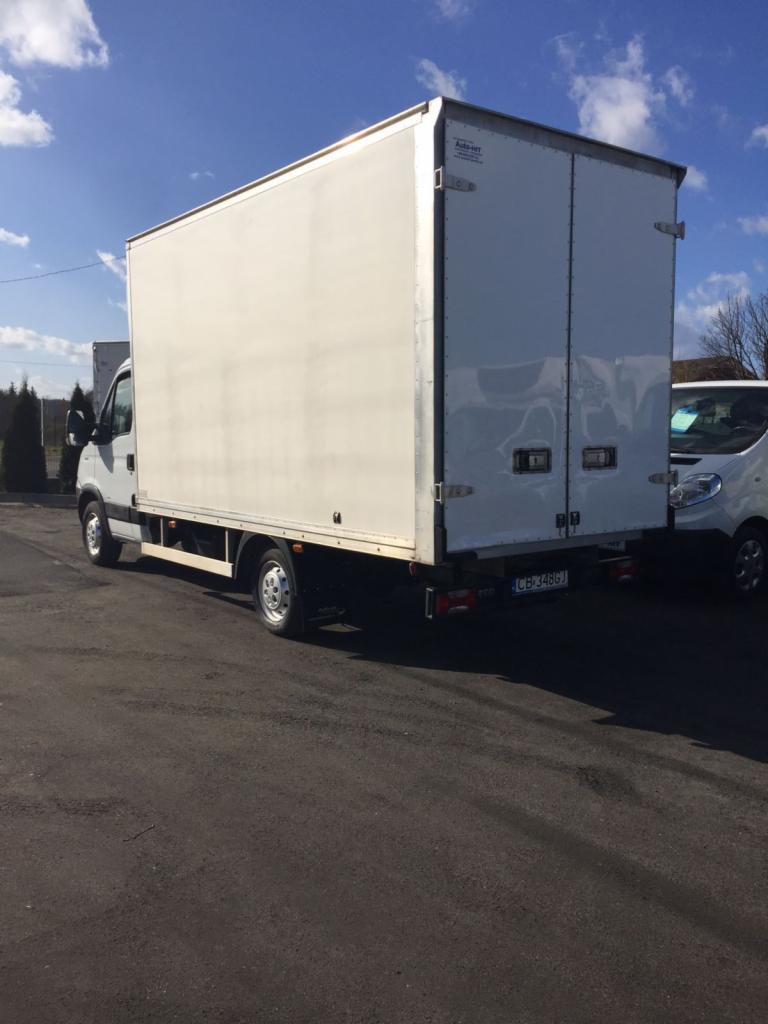 Biały samochód dostawczy z zabudową kontenerową, zaparkowany na asfalcie, widok z tyłu i boku, tablica rejestracyjna widoczna.