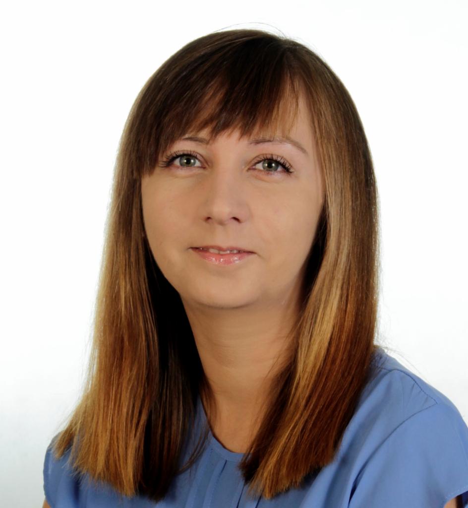 Portret uśmiechniętej kobiety z brązowymi włosami i niebieskiej bluzce na białym tle.