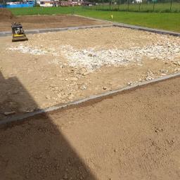 Rolka, Wykopy, Przyłącza, Transport - Przygotowany teren pod budowę z widocznymi fundamentami, częściowo utwardzony kruszywem, z ubijarką w tle i malowniczym krajobrazem górskim.