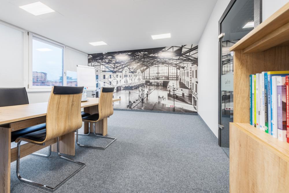 Nowoczesne biuro z drewnianym stołem, krzesłami i fototapetą przedstawiającą dworzec kolejowy w stylu retro.