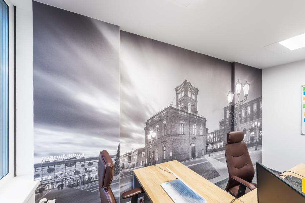 Biuro z fototapetą przedstawiającą czarno-biały widok na Manufakturę w Łodzi, widoczne biurka i krzesła.