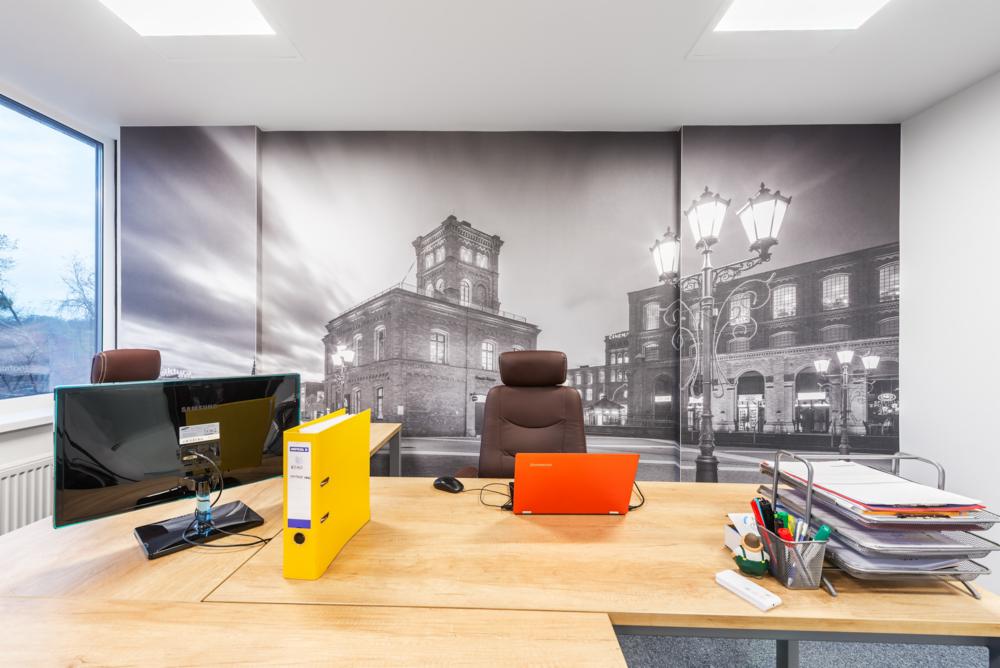 Biuro w Łodzi z fototapetą przedstawiającą budynek fabryki, biurko z laptopem i monitorem.