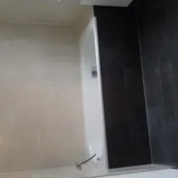 Wykończona łazienka z beżowymi i grafitowymi płytkami, widoczna wanna z zamontowaną baterią podtynkową.