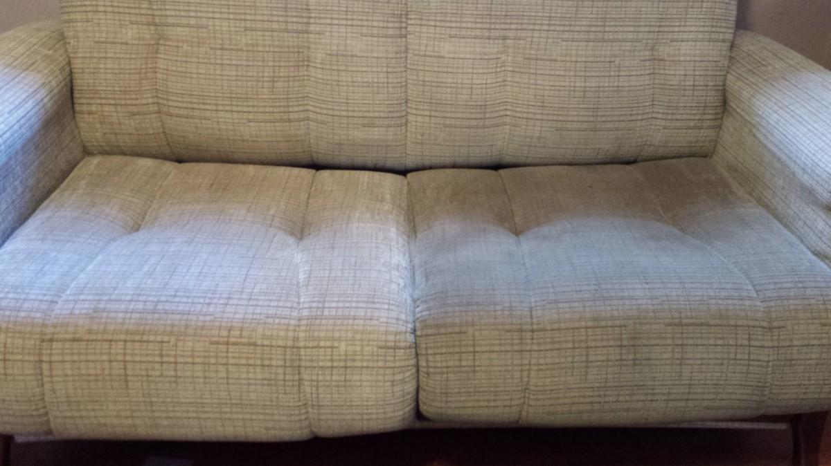 Dwuosobowa sofa tapicerowana tkaniną w kratkę, z widocznymi plamami i zabrudzeniami na siedzisku.