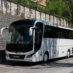 Biały autobus marki MAN zaparkowany wzdłuż kamiennego muru w słoneczny dzień.