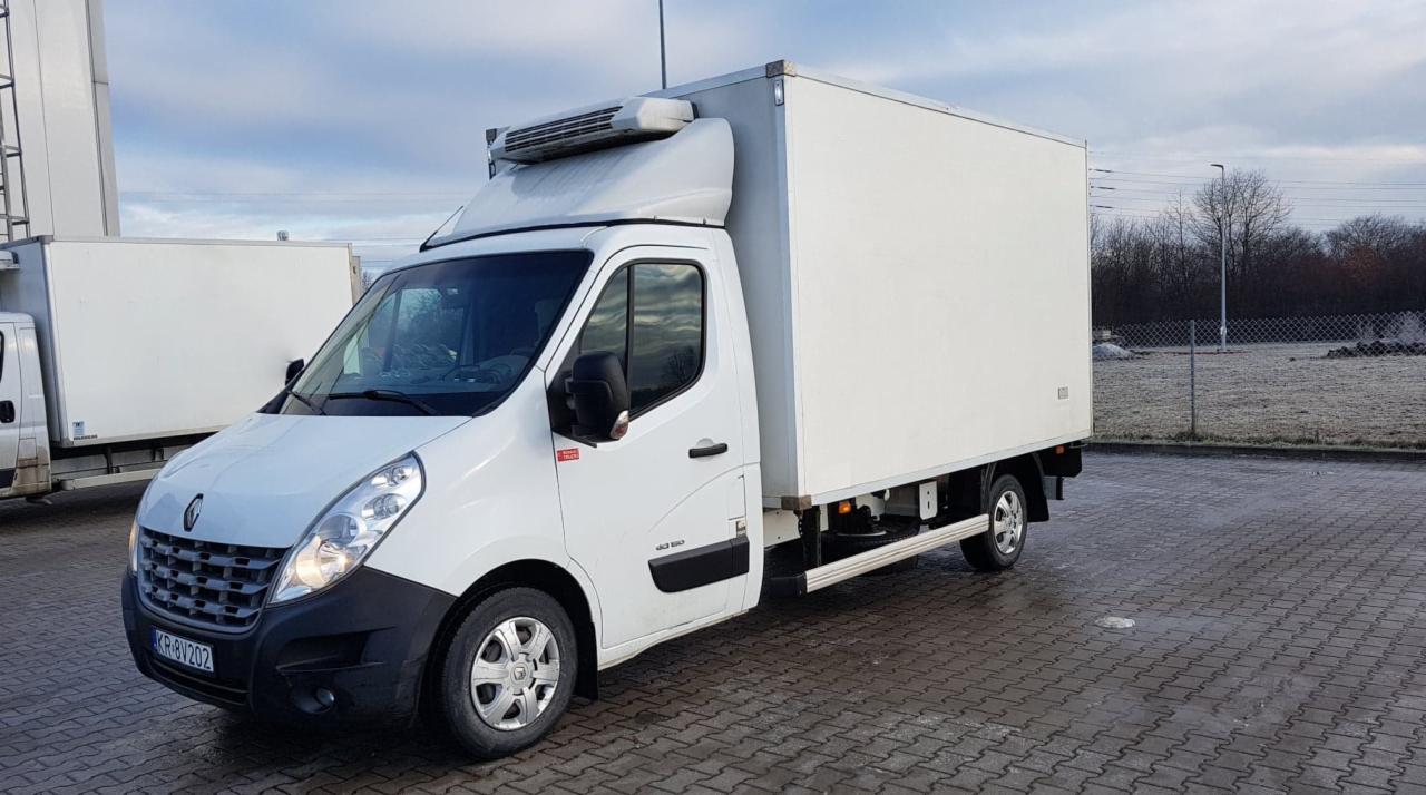 Biały samochód dostawczy Renault Master z chłodnią, zaparkowany na kostce brukowej w pochmurny dzień.