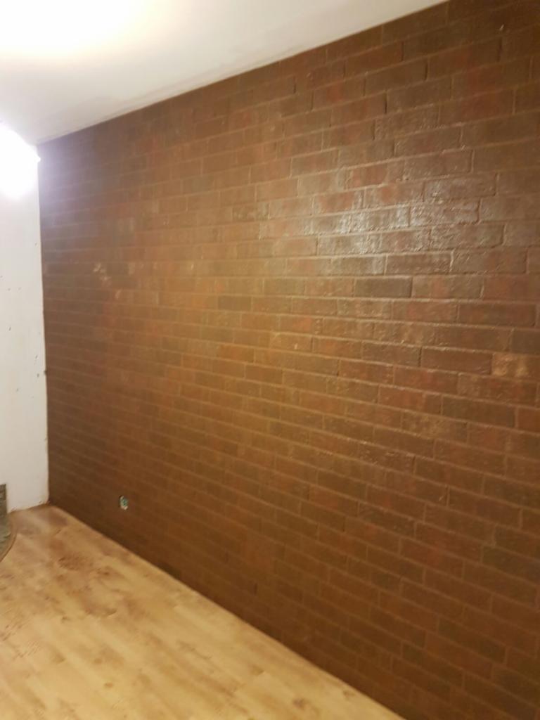 Ściana z efektem cegły w odcieniach brązu, wykończona błyszczącą powłoką, z panelami podłogowymi w jasnym odcieniu drewna.