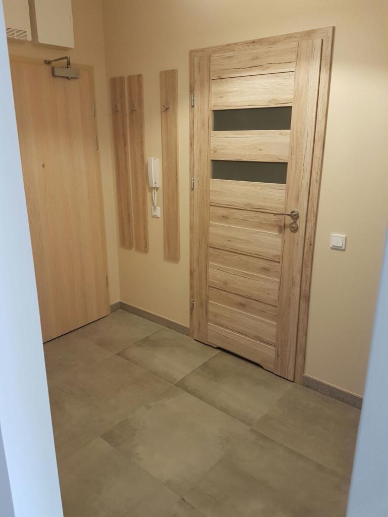 Wykończony przedpokój z drewnianą podłogą z płytek, drzwi wewnętrzne z przeszkleniami i wieszakami na ścianie.