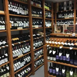 Półki wypełnione różnorodnymi butelkami wina w sklepie, z drewnianymi modelami pojazdów na jednej z półek.