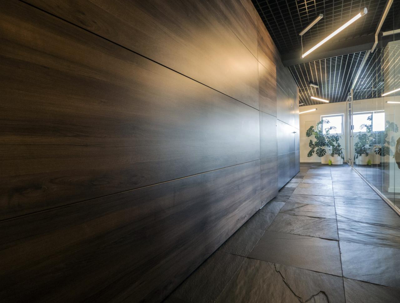 Długa szafa na wymiar z ciemnego drewna w biurze, z widoczną fakturą drewna i minimalistycznym designem, dopasowana do podłogi z kamiennych płyt.