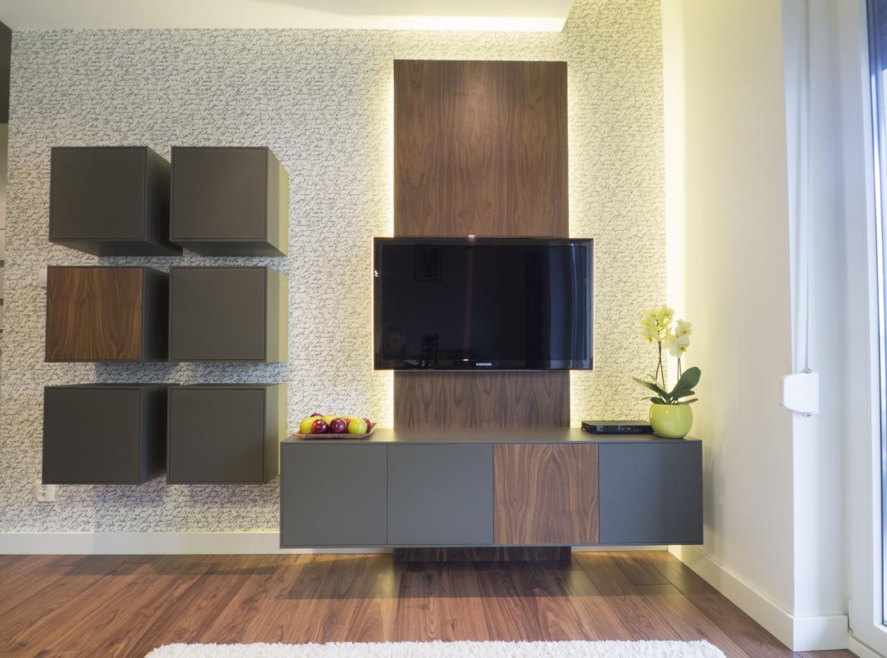 Nowoczesny salon z szafką RTV na wymiar, wiszącymi szafkami w kształcie kostek, podświetleniem LED i dekoracyjną tapetą w tle.
