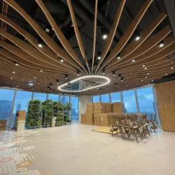 Nowoczesne biuro w wieżowcu z drewnianym sufitem rastrowym i nietypową lampą. Widok na miasto przez panoramiczne okna. Wykończenie wnętrz w trakcie.