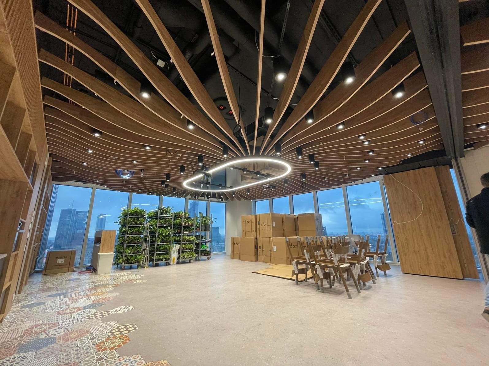 Nowoczesne biuro w wieżowcu z drewnianym sufitem rastrowym i nietypową lampą. Widok na miasto przez panoramiczne okna. Wykończenie wnętrz w trakcie.
