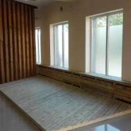 Wnętrze z drewnianą podłogą w trakcie montażu, widoczne listwy przypodłogowe z drewna i drewniana ścianka działowa z pionowych desek.