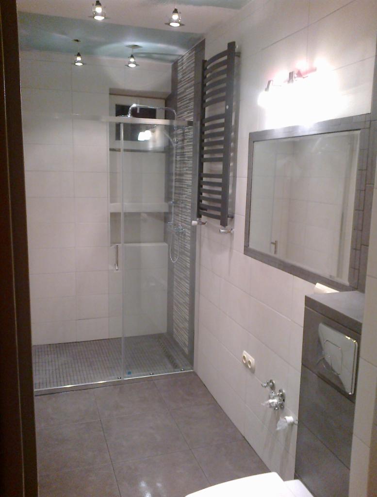 Nowoczesna łazienka z kabiną prysznicową typu walk-in, grzejnikiem drabinkowym i podtynkową toaletą, wykończona w jasnych płytkach z szarymi akcentami.