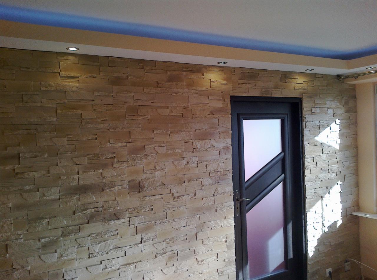 Ściana wykończona dekoracyjnym kamieniem piaskowcowym, z wbudowanymi punktowymi lampami sufitowymi i nowoczesnymi drzwiami z matową szybą, oświetlona z boku naturalnym światłem.