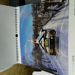 Otwarty kalendarz spiralny na styczeń 2019, prezentujący zimowy krajobraz z drewnianym kościołem w tle.