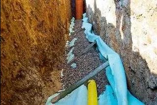 Wykop z ułożoną rurą drenarską, obsypany żwirem i zabezpieczony geowłókniną, widok z góry.