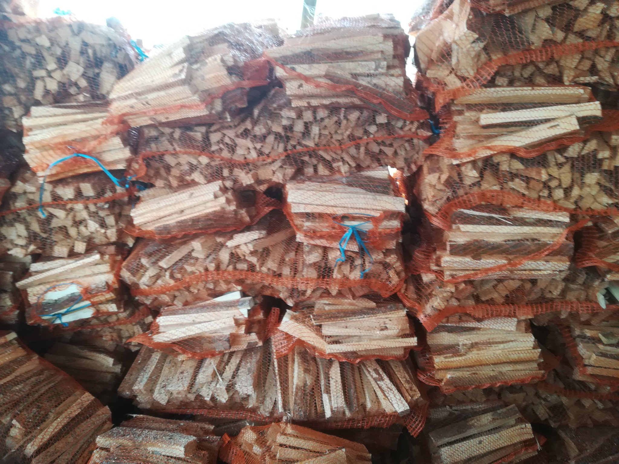 Stos worków raszlowych wypełnionych drobnym drewnem rozpałkowym sosnowym, ułożonych jeden na drugim.