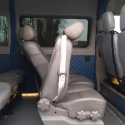 Wnętrze busa z szarymi skórzanymi siedzeniami, niebieską pikowaną tapicerką ścian i oświetleniem pod siedzeniami.