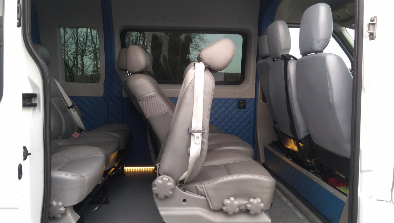 Wnętrze busa z szarymi skórzanymi siedzeniami, niebieską pikowaną tapicerką ścian i oświetleniem pod siedzeniami.