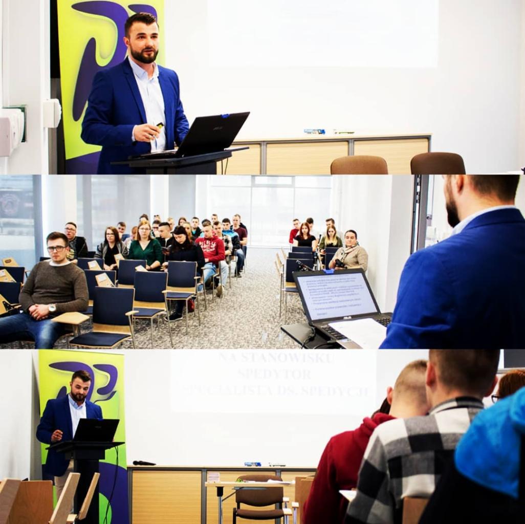 Prezentacja szkoleniowa z zakresu spedycji: mężczyzna w niebieskiej marynarce przemawia do grupy osób siedzących w rzędach, na ekranie wyświetlony napis 'Na stanowisku spedytor, specjalista ds.