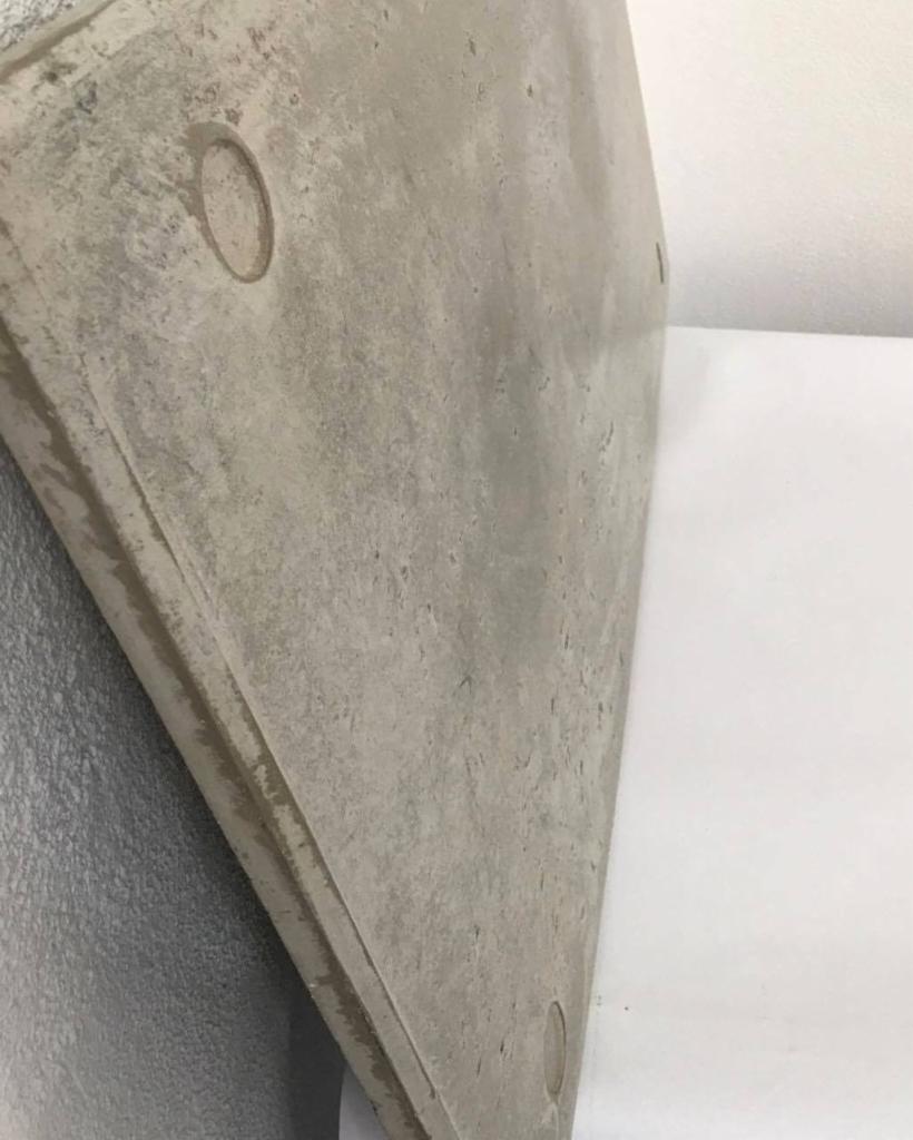 Płyta z betonu architektonicznego, widok z boku, z widocznymi porami i drobnymi niedoskonałościami powierzchni, na tle białej ściany.