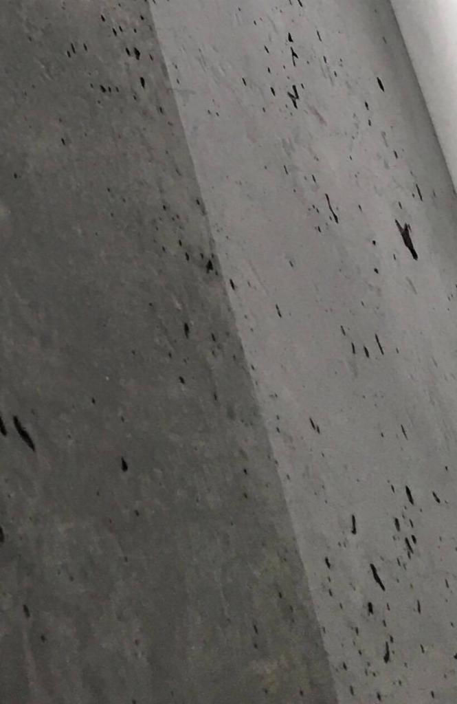 Szara płyta z betonu architektonicznego z ciemnymi plamkami, ujęcie pod kątem, widoczny fragment krawędzi płyty.