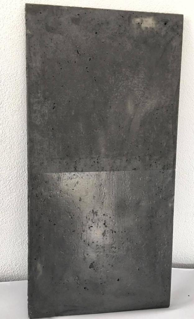 Płyta z betonu architektonicznego w odcieniach szarości, z widoczną fakturą i drobnymi porami, o nierównomiernym wykończeniu powierzchni, gdzie górna część jest matowa, a dolna odbija światło.