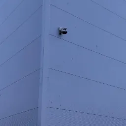 Kamera monitoringu zamontowana na szarej elewacji budynku z widocznym logo firmy na górze