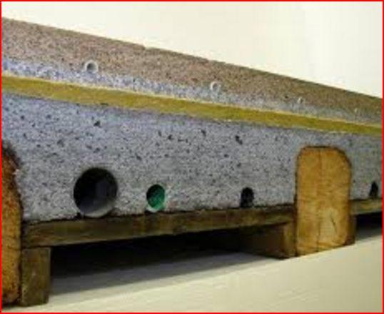 Przekrój betonowej belki stropowej z widocznymi warstwami izolacji, otworami na instalacje i drewnianą konstrukcją wsporczą.