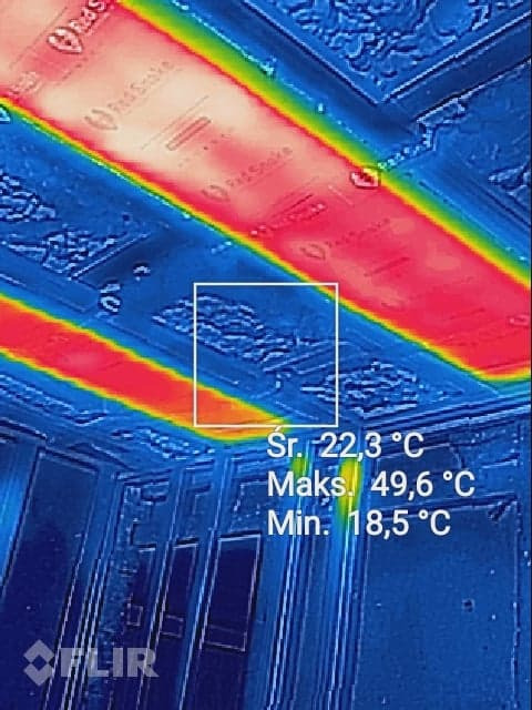 Termowizyjne zdjęcie sufitu z zaznaczonymi strefami o różnej temperaturze, wskazujące na potencjalne straty ciepła. Widoczne wartości minimalne, średnie i maksymalne temperatury oraz logo...