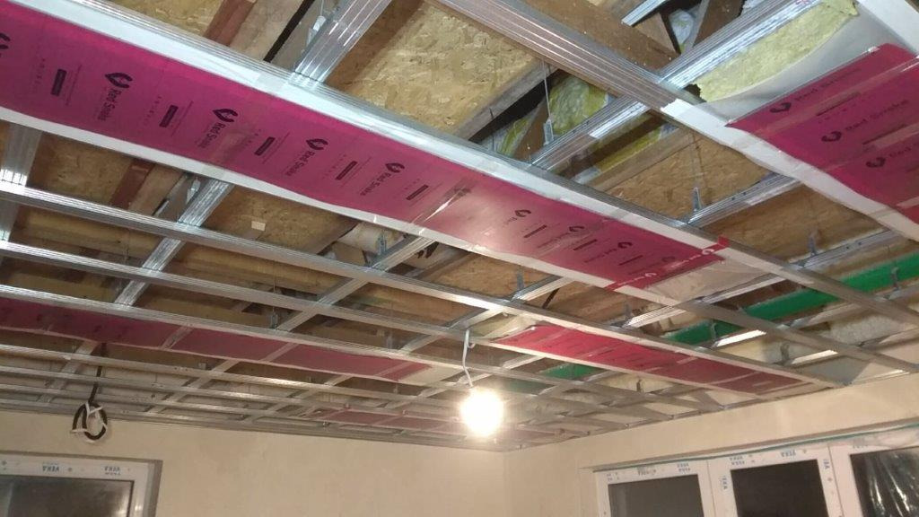 Montaż sufitu podwieszanego z widoczną konstrukcją metalową, izolacją i elementami instalacji wentylacyjnej w budynku w trakcie wykończenia.